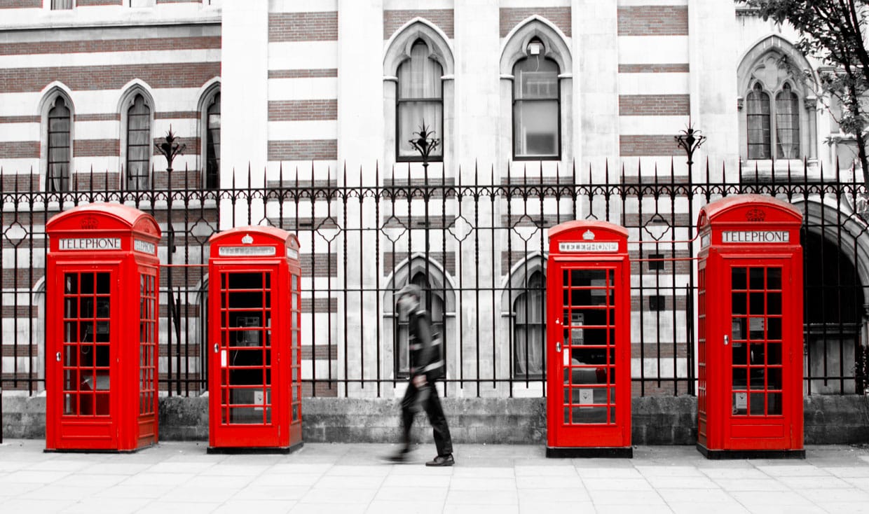 Someone walking in front of multiple red phone booth in London, UK